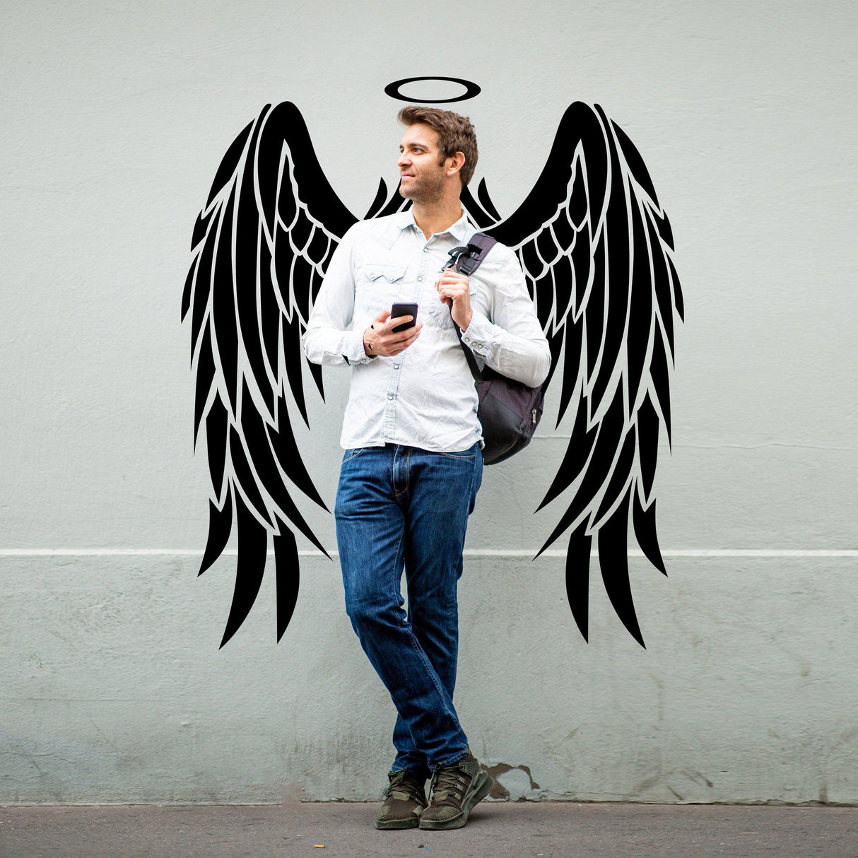 Man standing by angel wings vinyl decal, showcasing elegant wall decor for a stylish touch.