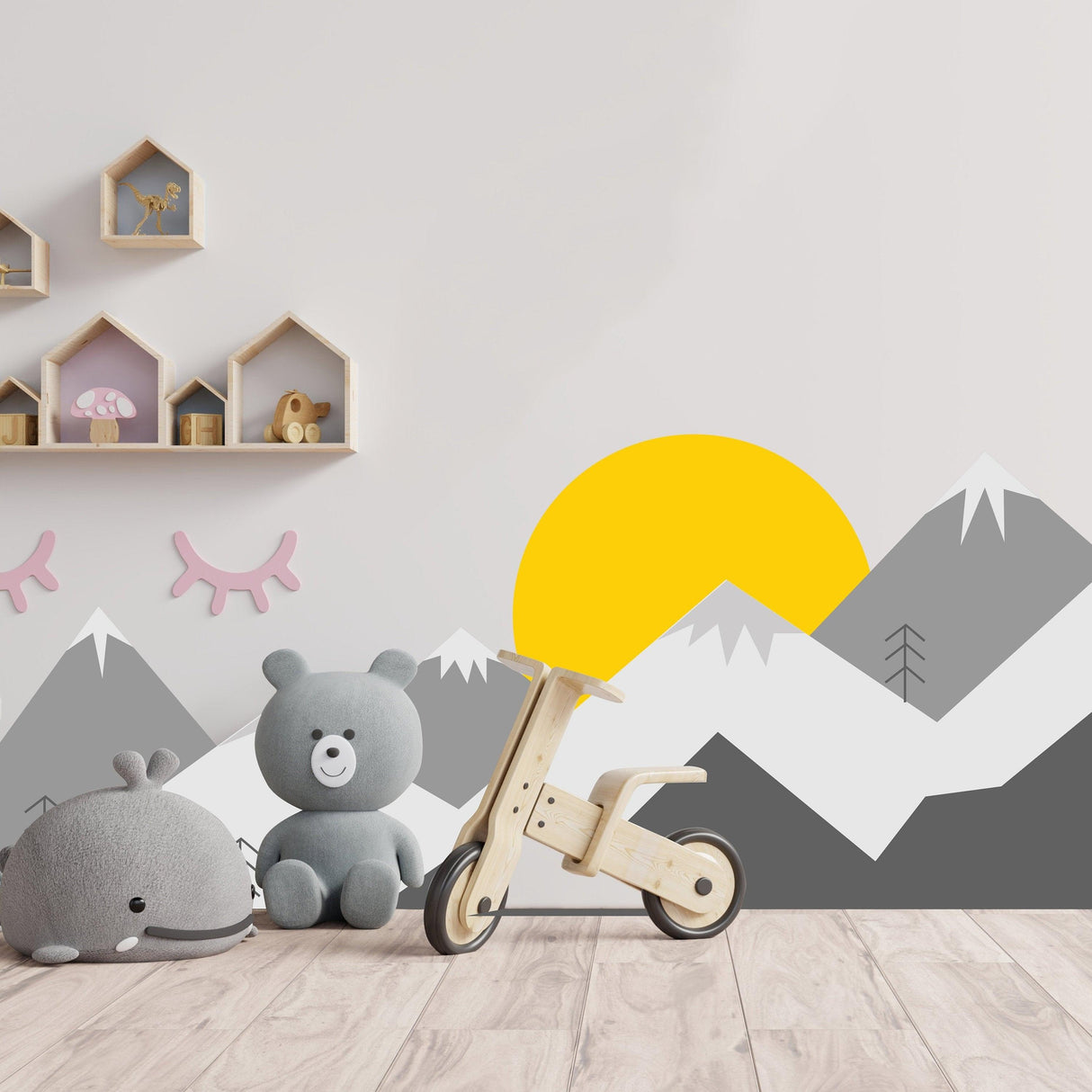 Mountain wall decal in a nursery with toys and decor, featuring a sun and gray mountains.