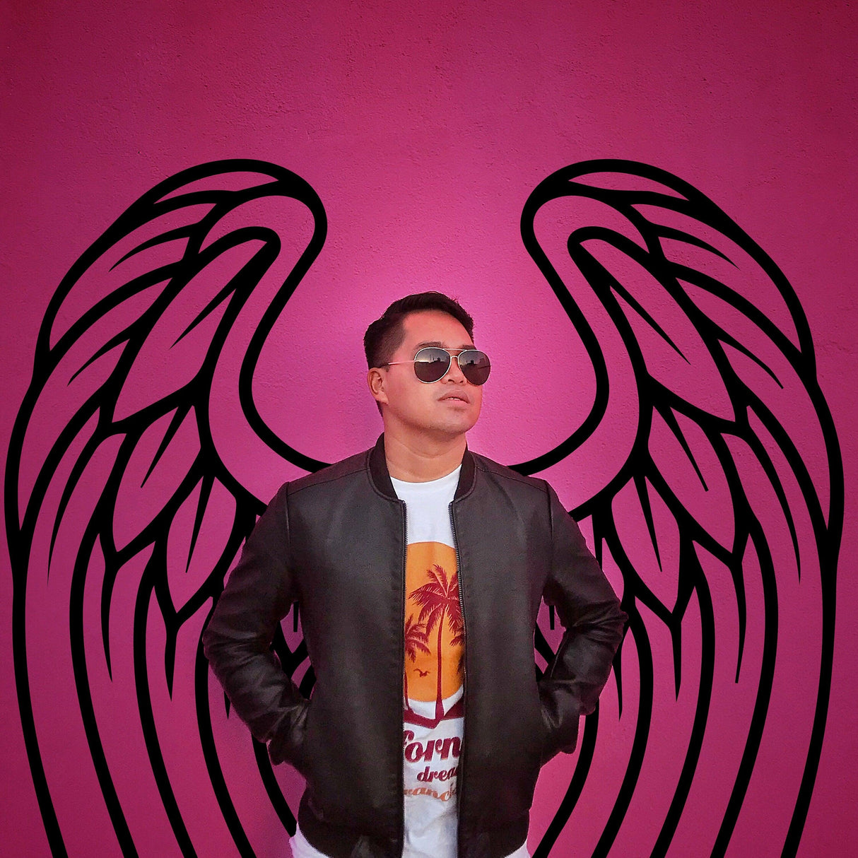 Person in sunglasses standing against a vibrant pink wall with angel wings design, showcasing stylish urban decor.