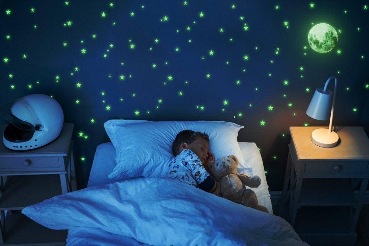 Child peacefully sleeping under glow in the dark star stickers and moon decal in a cozy nursery.