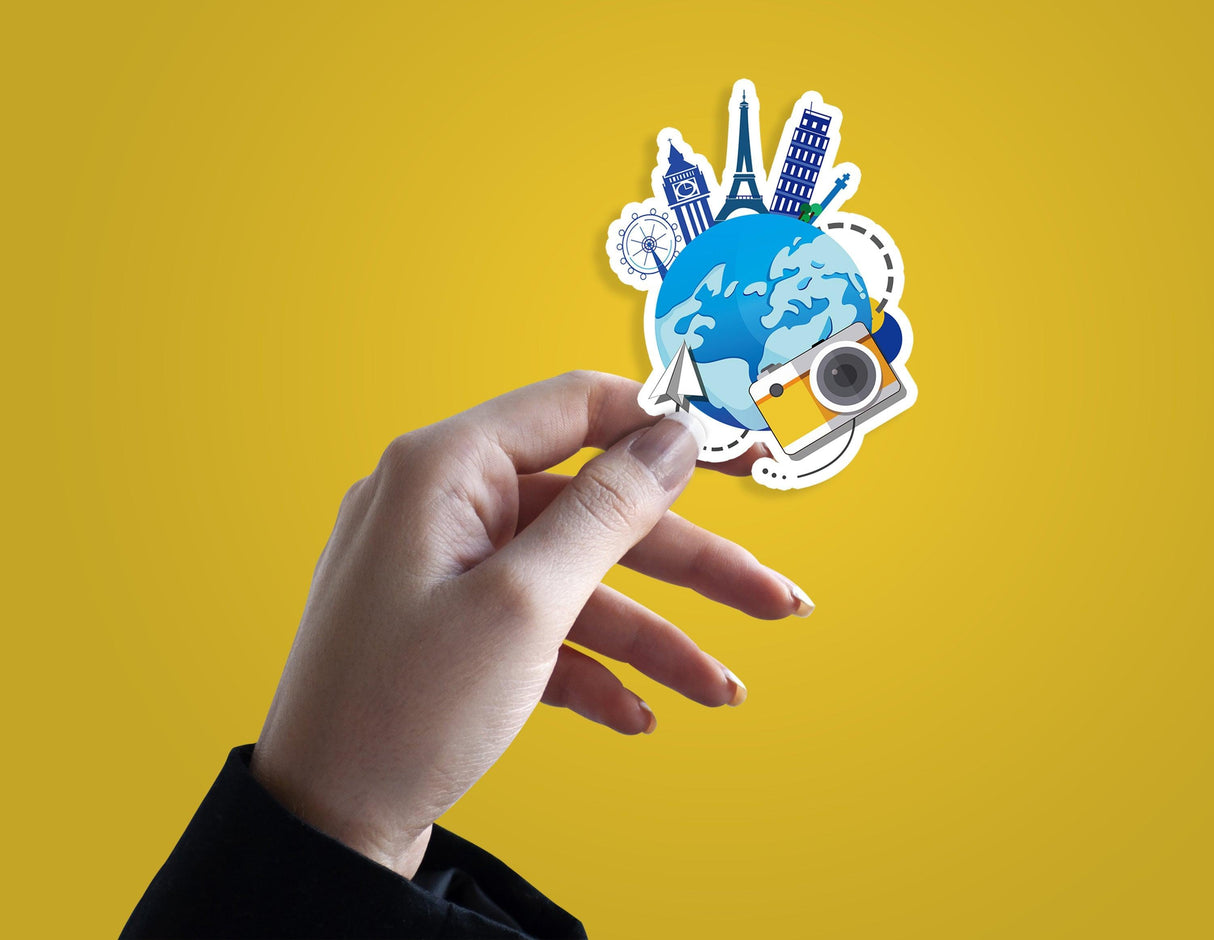 Hand holding a colorful travel-themed die cut vinyl sticker featuring landmarks and a globe.