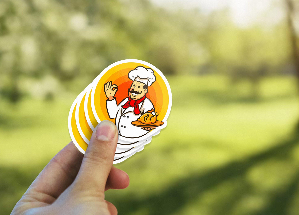 Hand holding colorful chef vinyl stickers with a cheerful design against a bright outdoor background.
