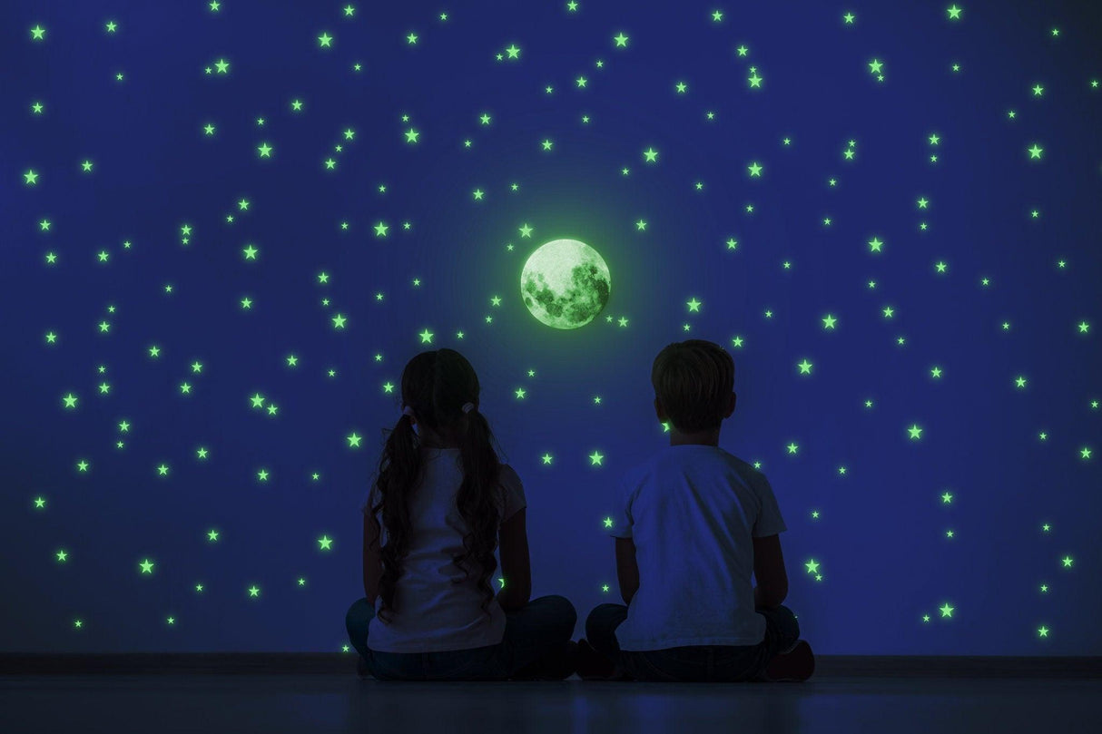 Children sitting against a wall decorated with glow-in-the-dark stars and a glowing moon decal.