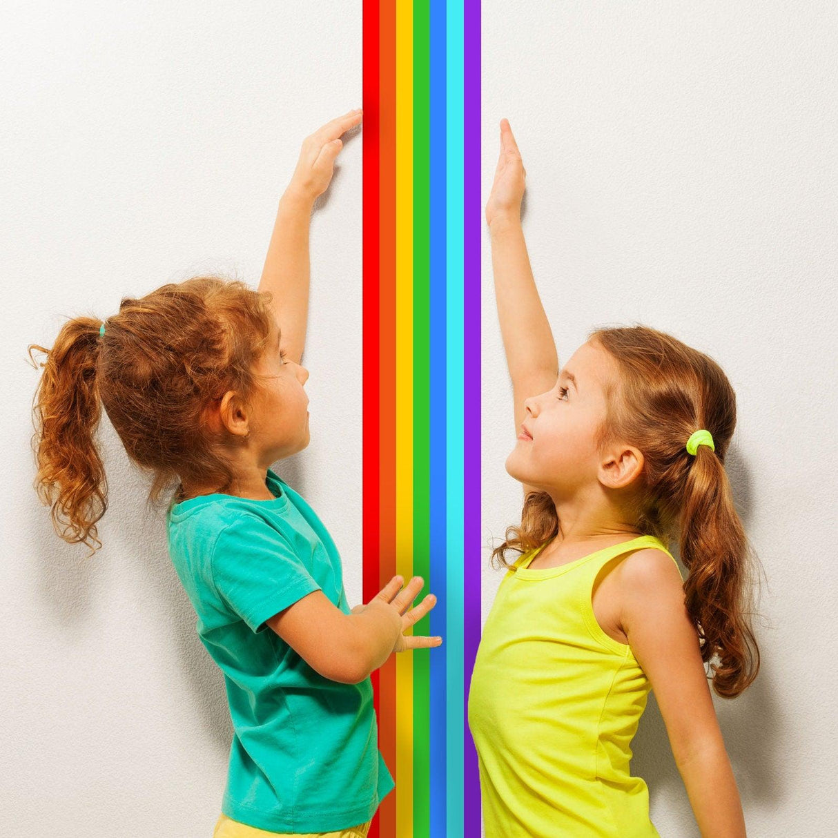 Two children reaching for a colorful rainbow border sticker on a white wall, adding playful decor to their room.