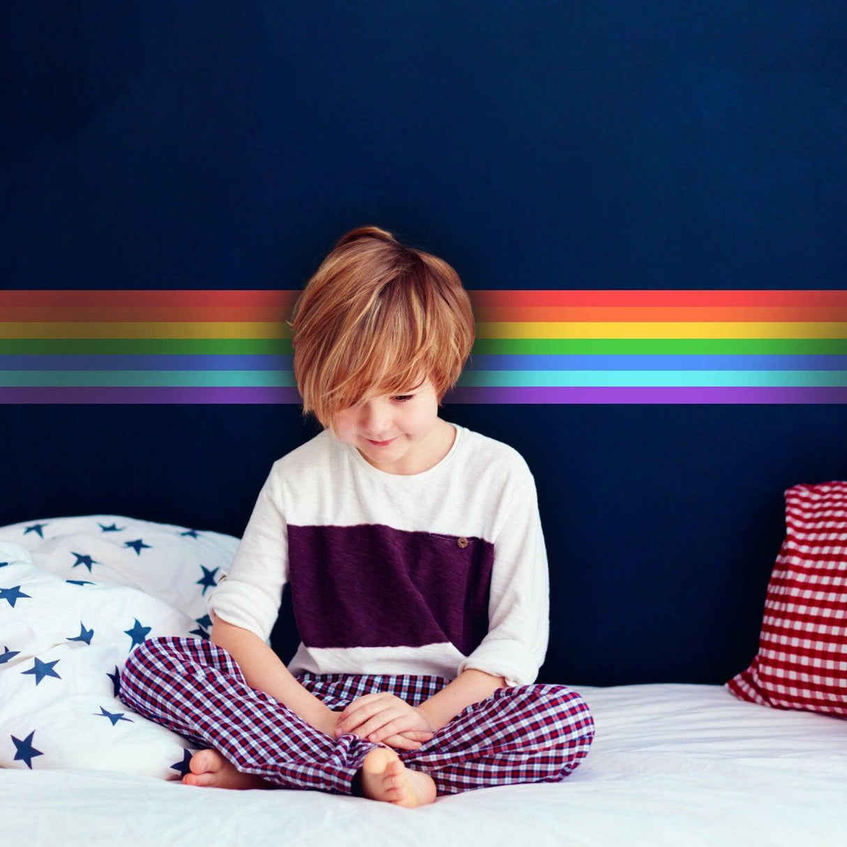 A child sitting on a bed with rainbow stripe wall decal, creating a colorful and playful nursery atmosphere.