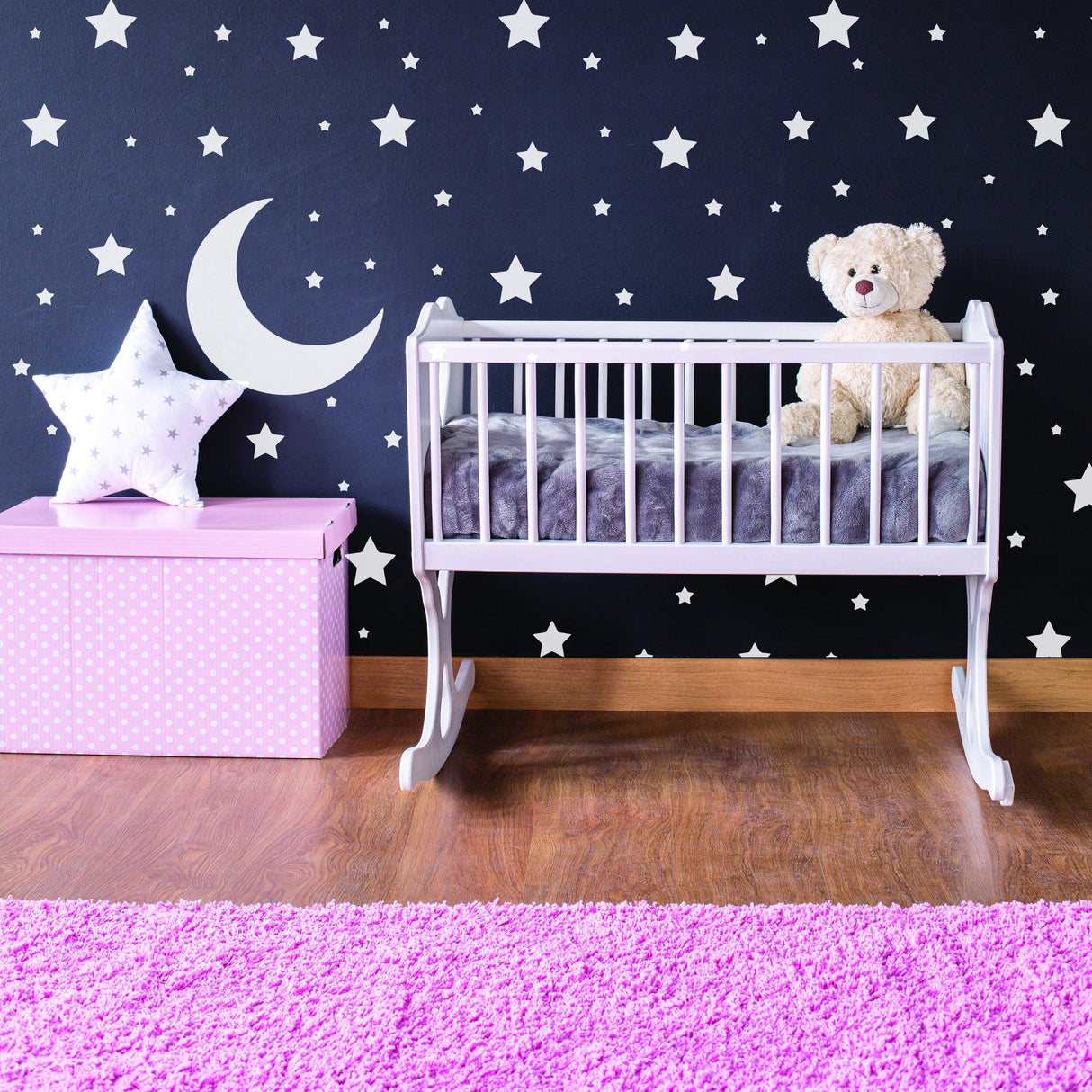 Nursery featuring Stars Wall Decals Pack, crib with teddy bear, and pink star decor on black wall.