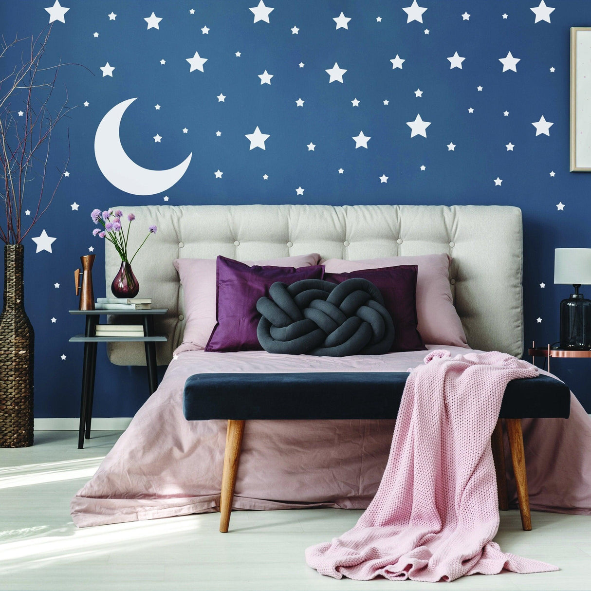 A cozy nursery room with navy walls decorated with stars and a moon, featuring a stylish bed and soft textiles.