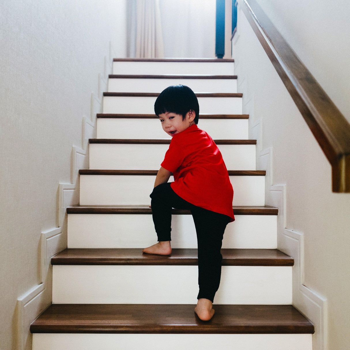 Young child in a red shirt climbing self-adhesive white stairs risers stickers, showcasing a vibrant staircase.