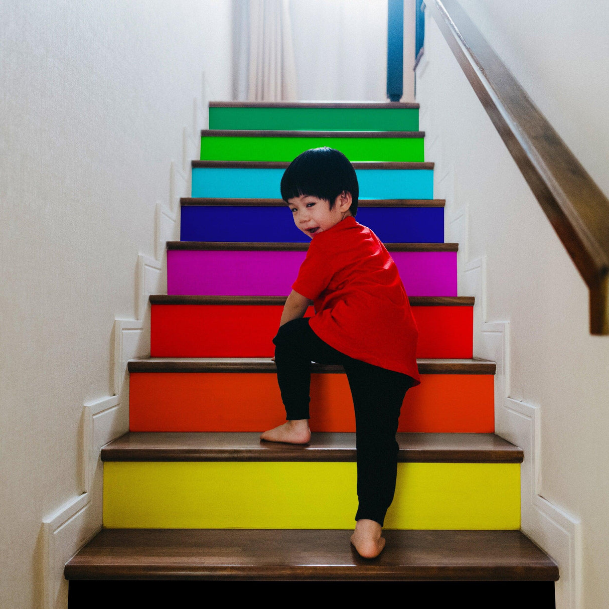 Child climbing colorful rainbow self-adhesive stairs risers stickers, adding vibrancy and fun to the staircase.