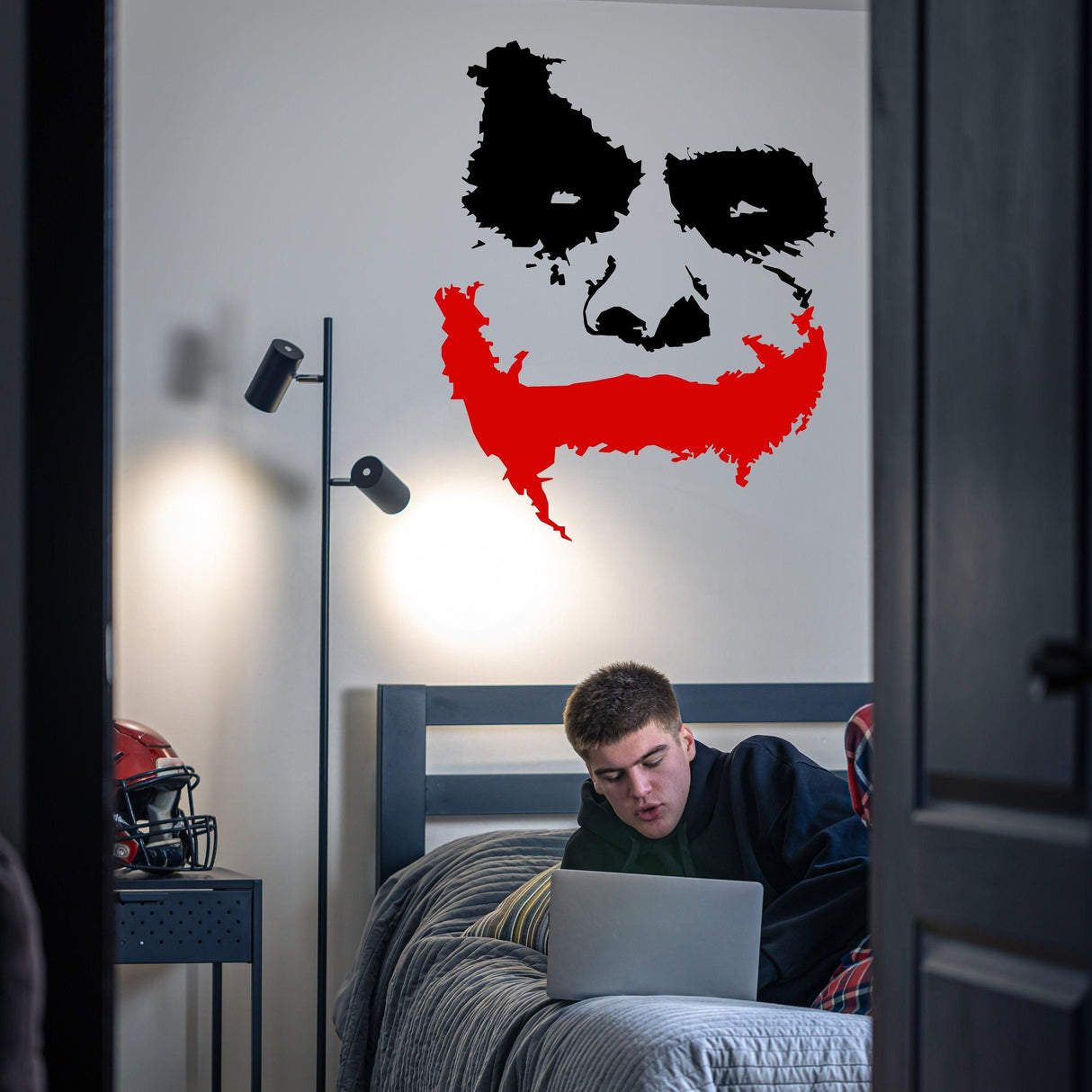 Joker wall sticker with red accents on bedroom wall, featuring a smiling clown face, for decorative flair.