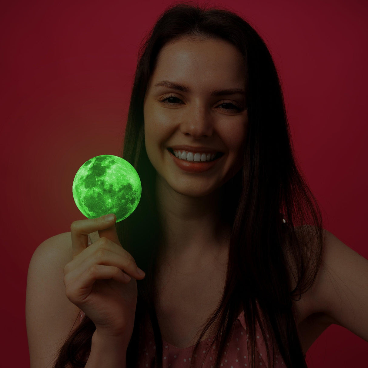 Happy woman holding a glowing green full moon sticker against a pink background.