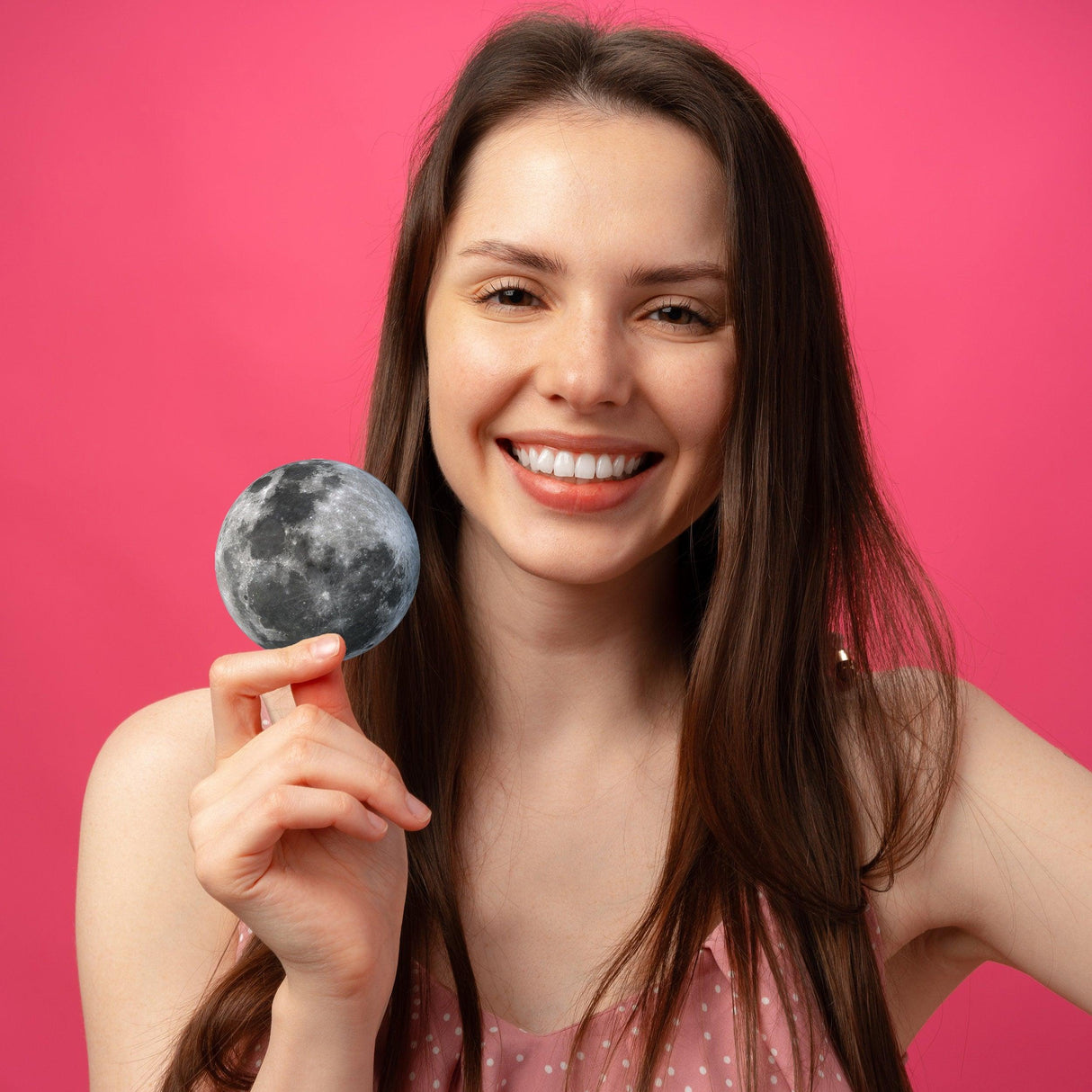 Smiling woman holding a glowing full moon vinyl decal against a pink background.