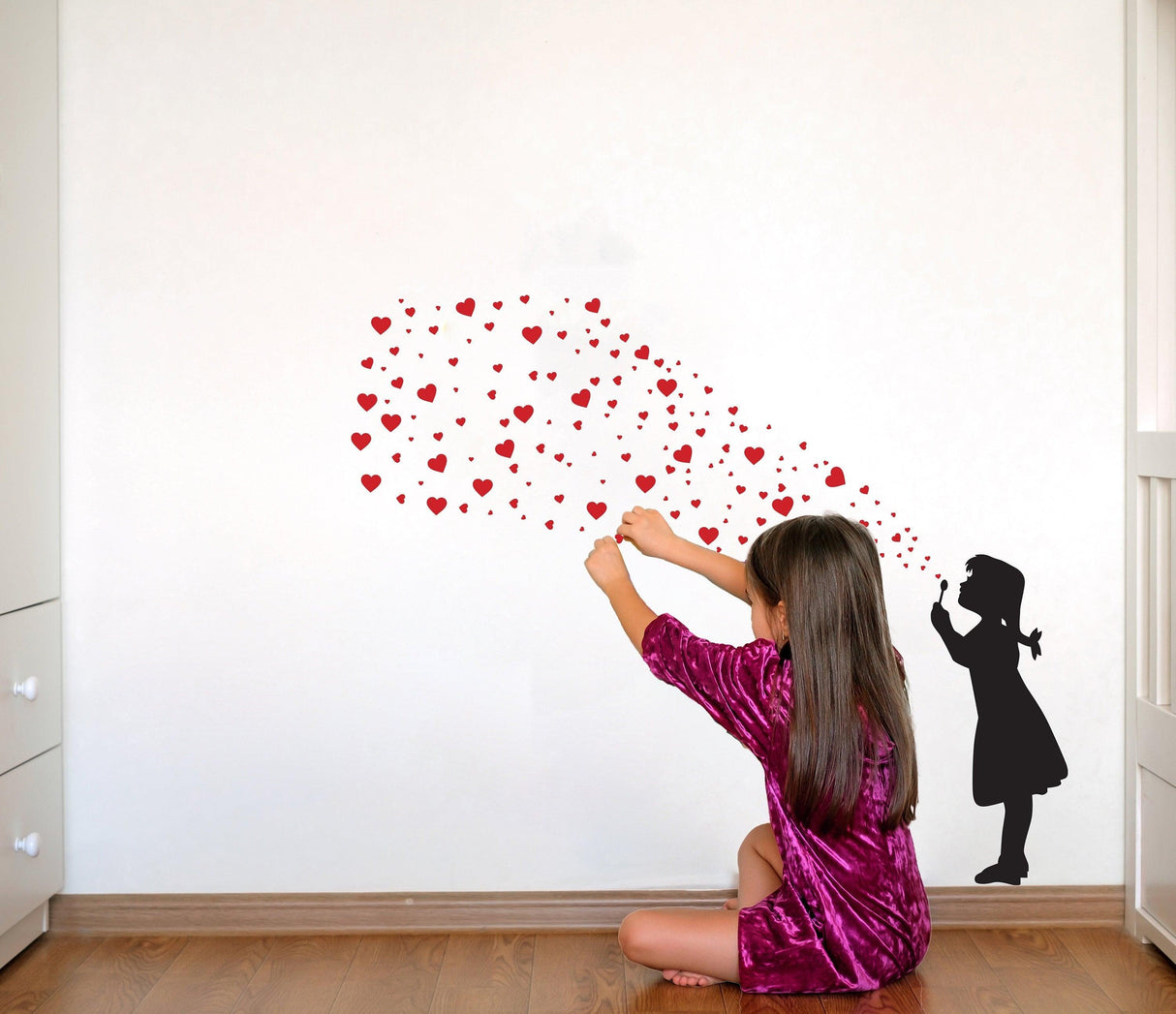Girl in a purple dress sitting and blowing heart-shaped bubbles on a wall, creating a playful and colorful decor.