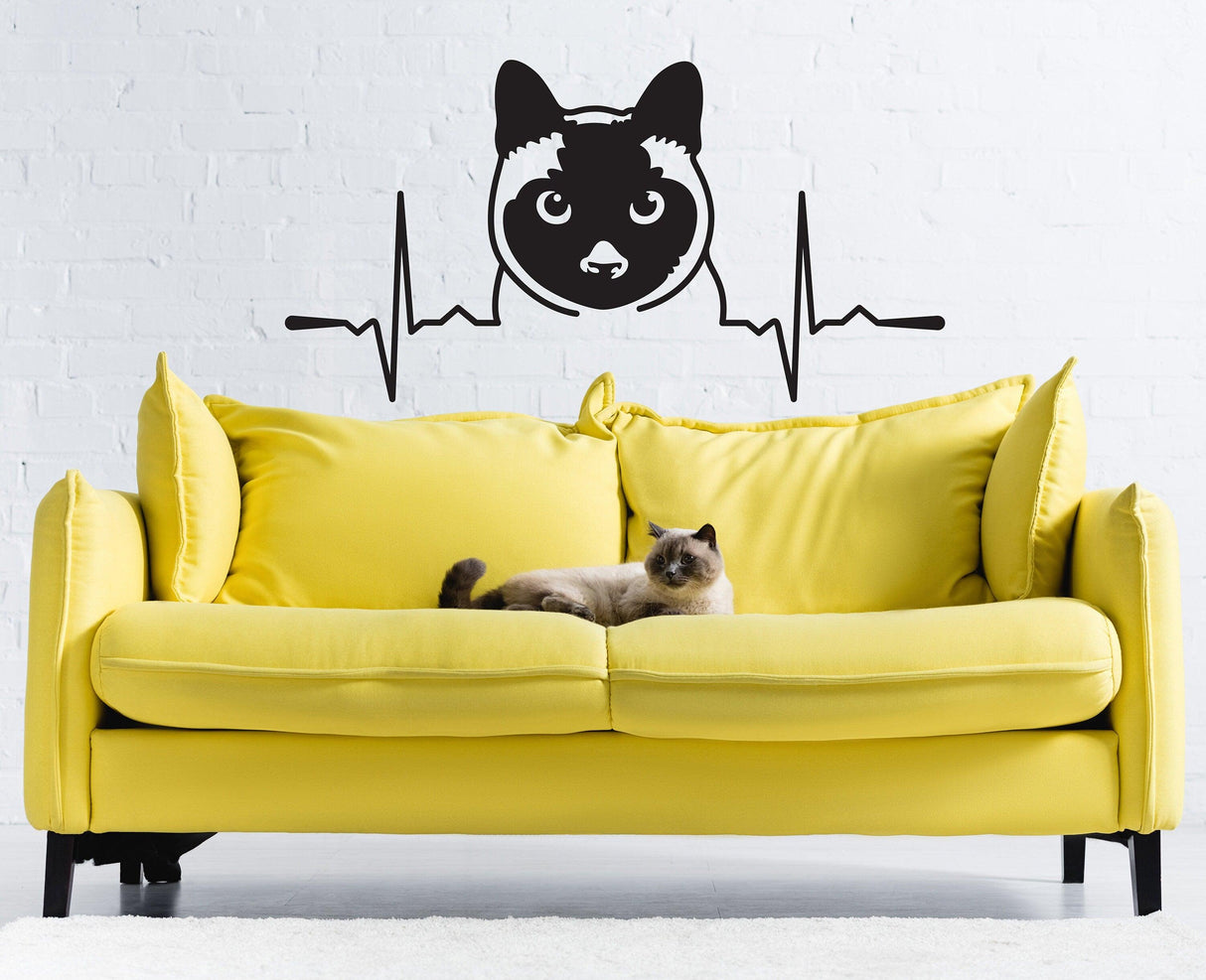 Siamese cat wall decal above a yellow couch with a real Siamese cat lounging on it.