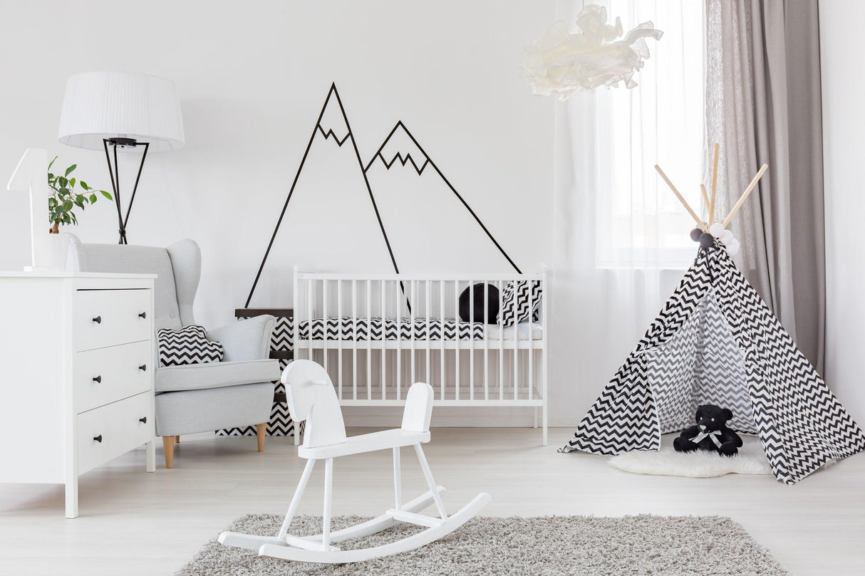 Stylish nursery with black mountain wall decals, crib, rocking chair, and playful teepee decoration.