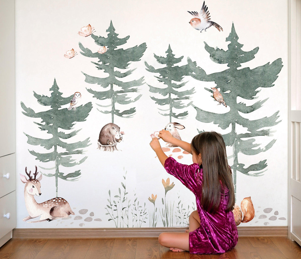 Child applying Forest Animals and Trees wall decal in a nursery, featuring watercolor trees and woodland creatures.