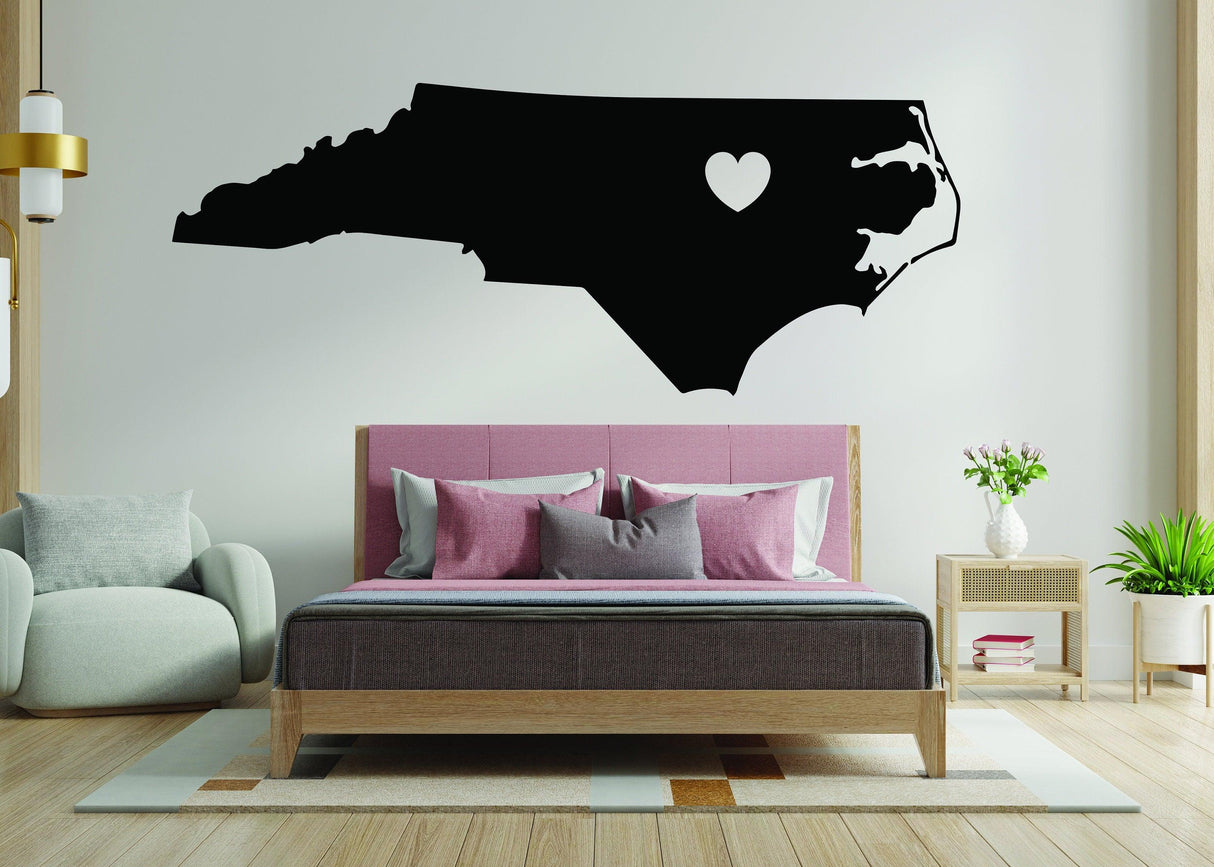 Black North Carolina wall decal with heart, perfect for NC state lovers, displayed above a stylish bed.