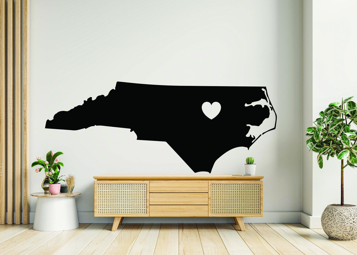 Black vinyl wall decal of North Carolina with a heart cutout, perfect for showing Tar Heel state pride in home decor.