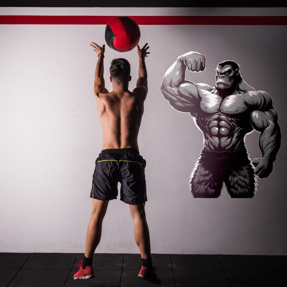 Man exercising with medicine ball next to a muscled gorilla wall decal for gym motivation.