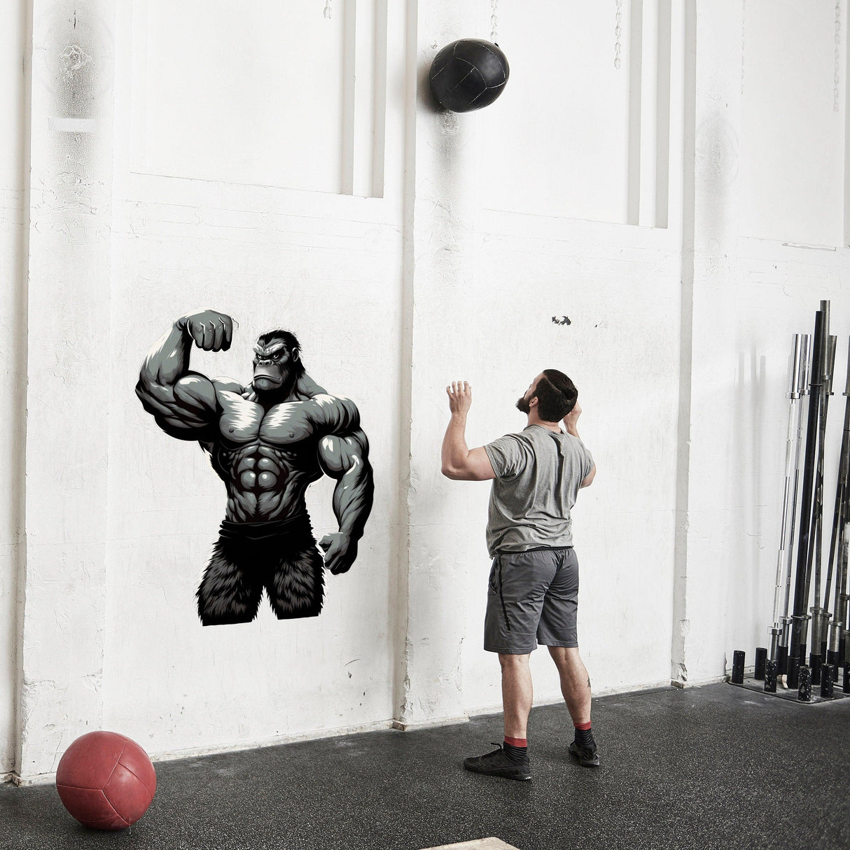 Muscled gorilla wall decal inspiring gym motivation with a man in workout attire throwing a ball.