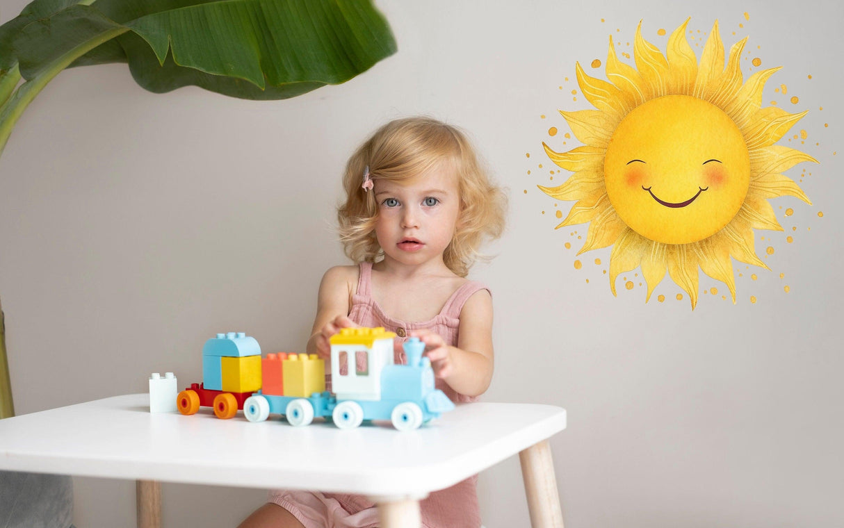 A cheerful girl playing with a toy train next to a vibrant watercolor sun wall sticker in a bright nursery.