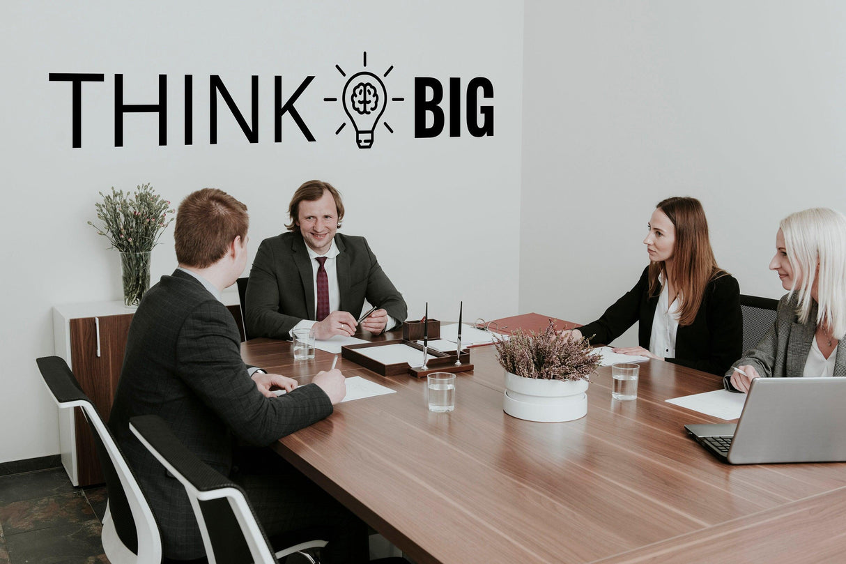 Four professionals in a conference room discussing, with 'THINK BIG' decal on the wall, inspiring workplace decor.