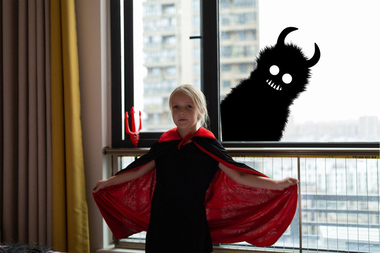 Girl in a red cape with a monster shadow sticker in the window for Halloween decorations.