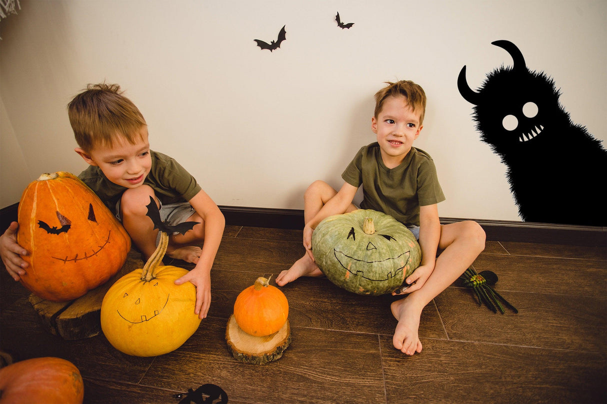 Two young boys seated with Halloween pumpkins, spooky monster decoration in the background.