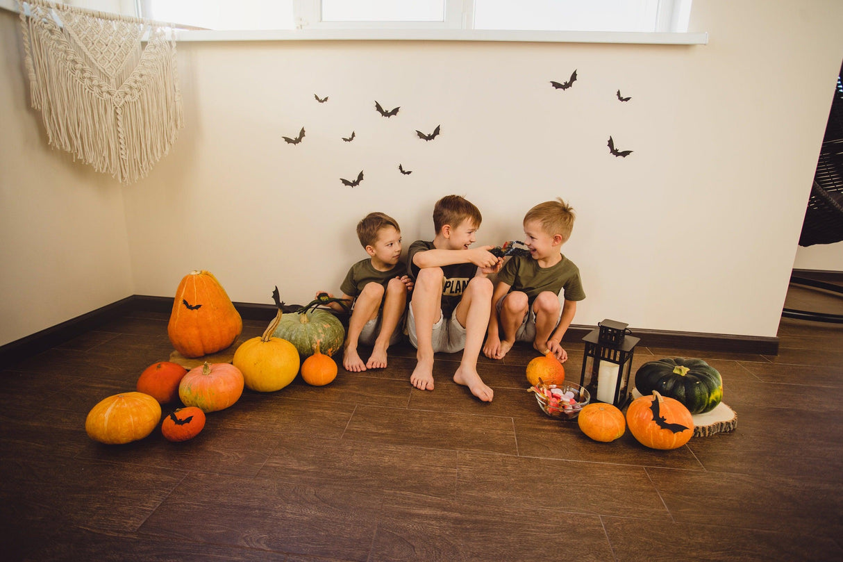 Three children sitting on the floor with Halloween bat window stickers and decorative pumpkins.