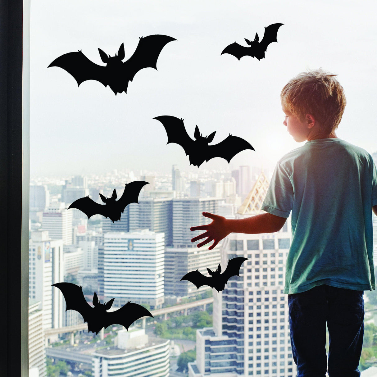 Child admiring Halloween bats window decals against a city skyline, perfect for October 31st decorations.