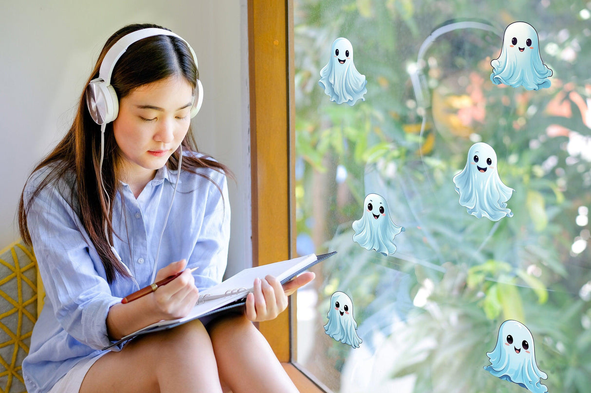 A girl wearing headphones sits by a window, drawing with spooky white ghost decals on the glass.