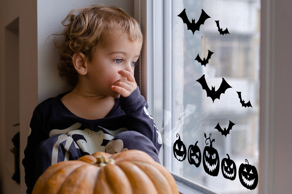 Child looking at Halloween window decals featuring bats and pumpkins, with a pumpkin in the foreground.