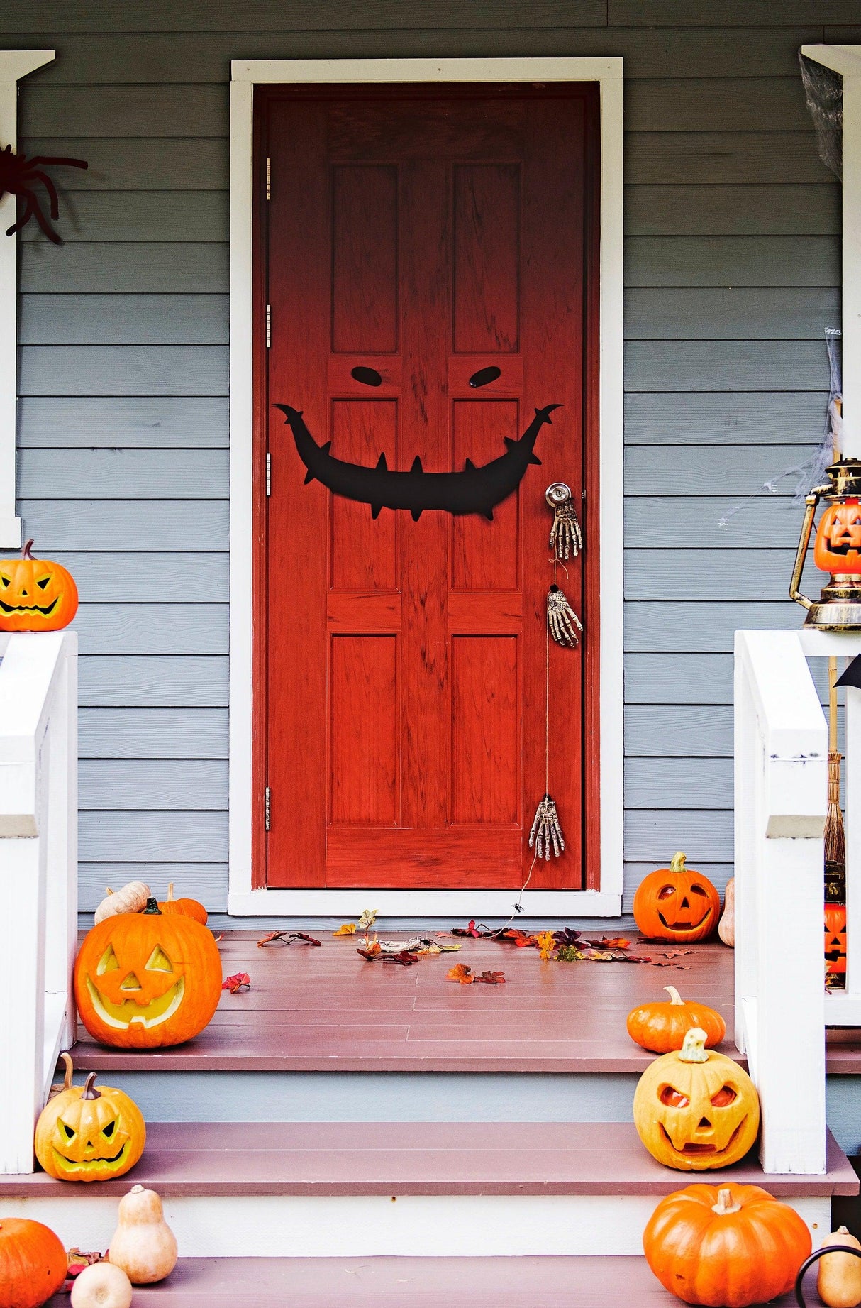 Halloween door decorated with a scary smile decal, surrounded by pumpkins and fall leaves.