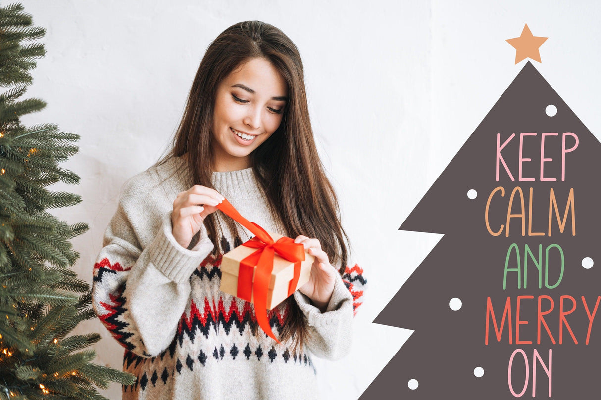 Woman in a cozy sweater opening a gift with a festive Christmas tree and 'Keep Calm and Merry On' decal.