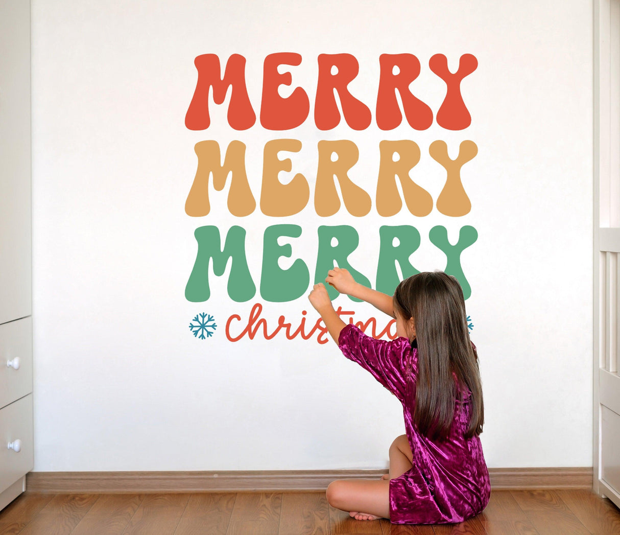 Child applying a colorful 'Merry Merry Merry Christmas' wall decal in a cozy room setting.