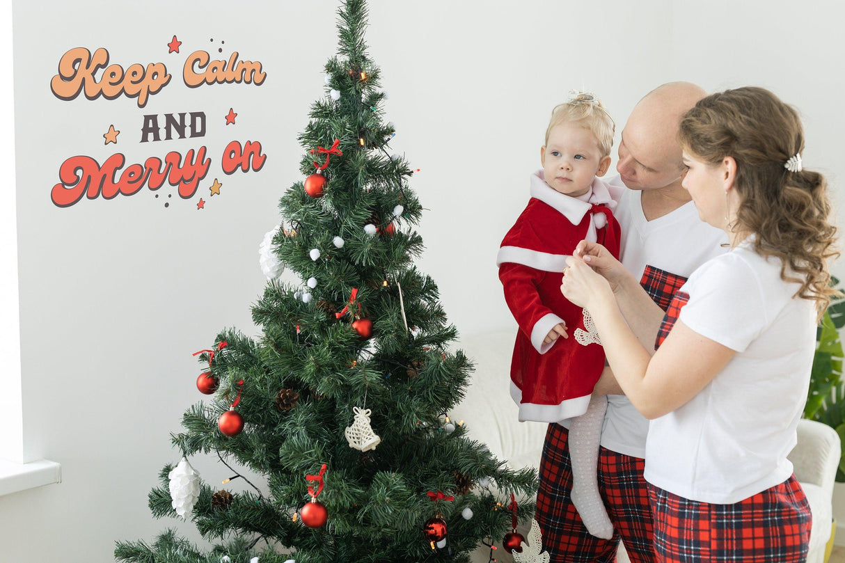 Happy family decorating a Christmas tree with whimsical 'Keep Calm and Merry On' decal in the background.
