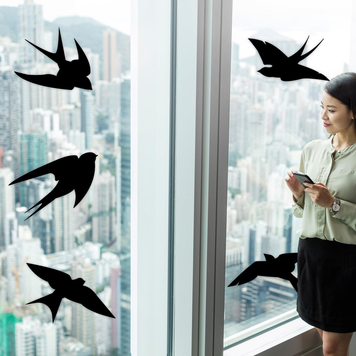 Woman standing by a window with black bird silhouette decals, enhancing bird safety and reducing collisions.