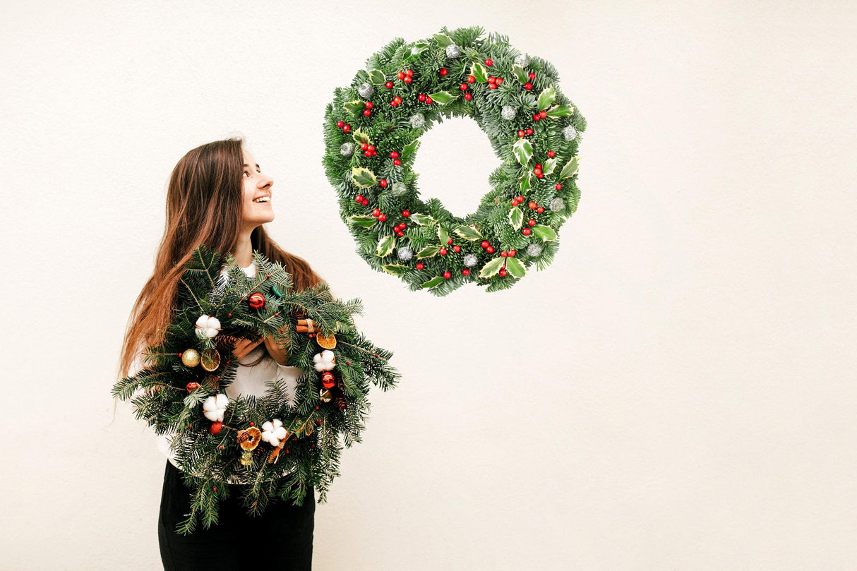 Woman smiling with Christmas wreaths, showcasing green leaves and red berries decorations.