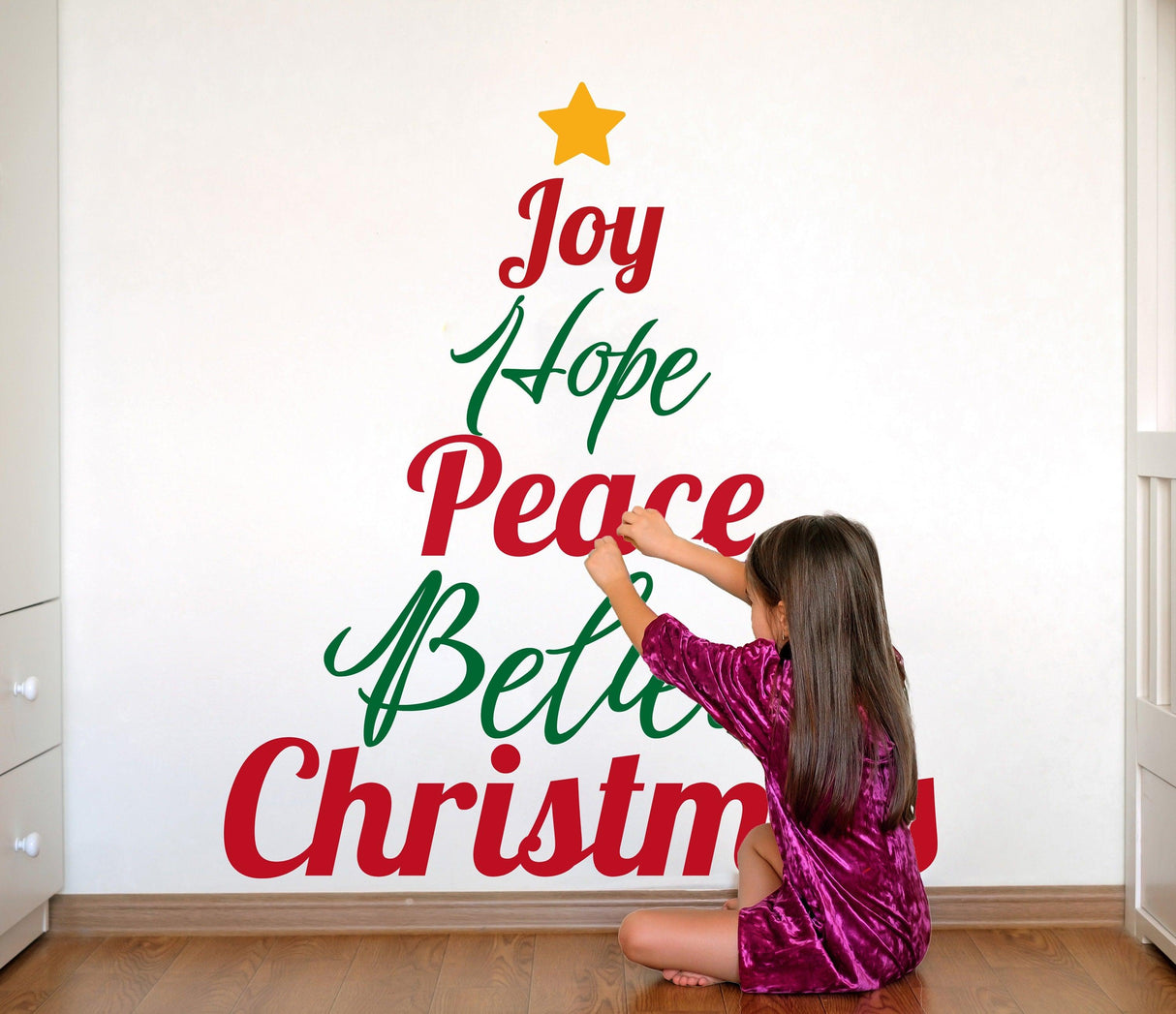 Child decorating a wall with a colorful Christmas quote decal saying 'Joy Hope Peace Believe Christmas'.