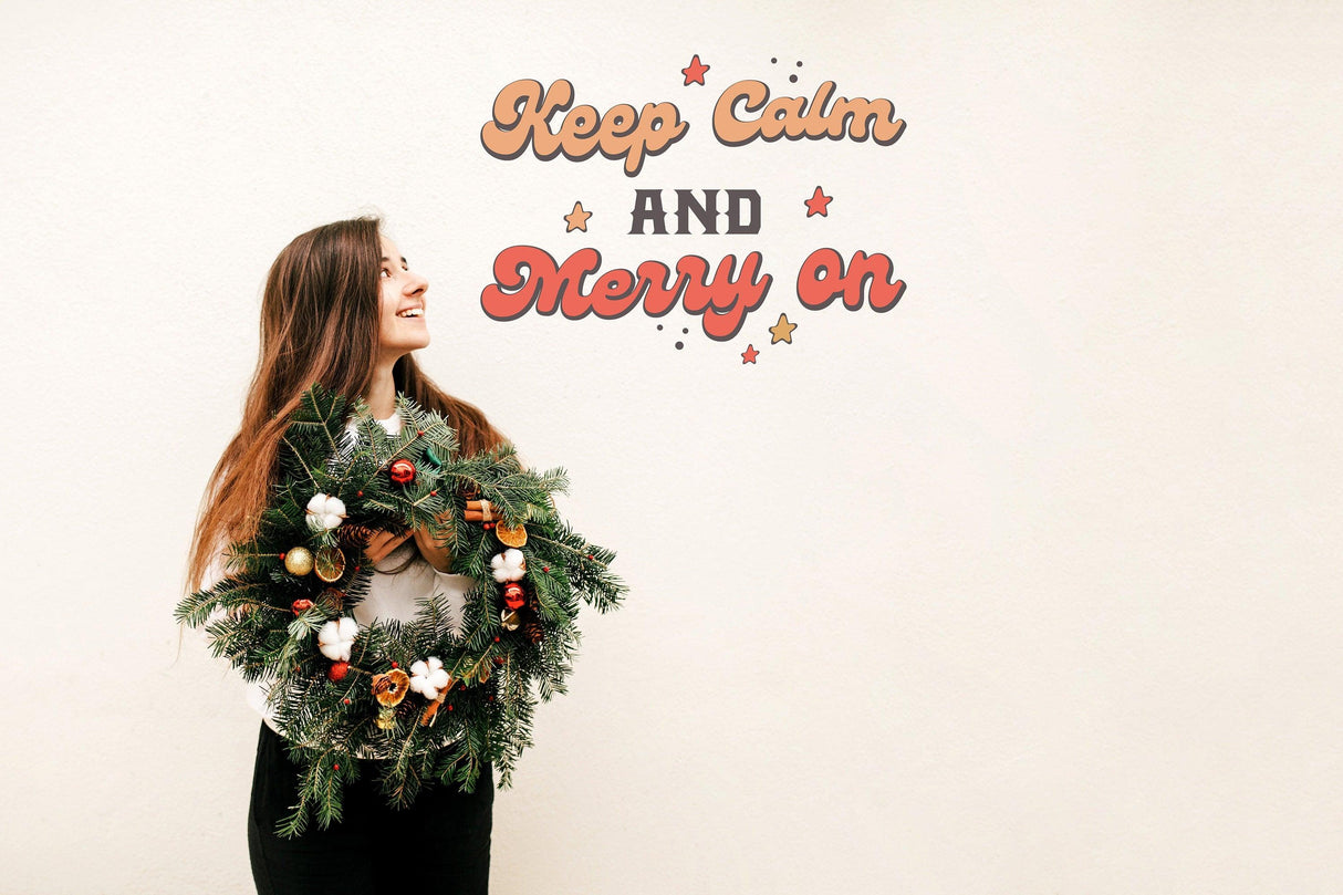 Woman holding a festive wreath under the 'Keep Calm and Merry On' colorful wall decal.