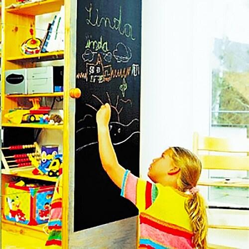 Child drawing on a chalkboard wall decal in a vibrant, organized playroom with colorful toys.