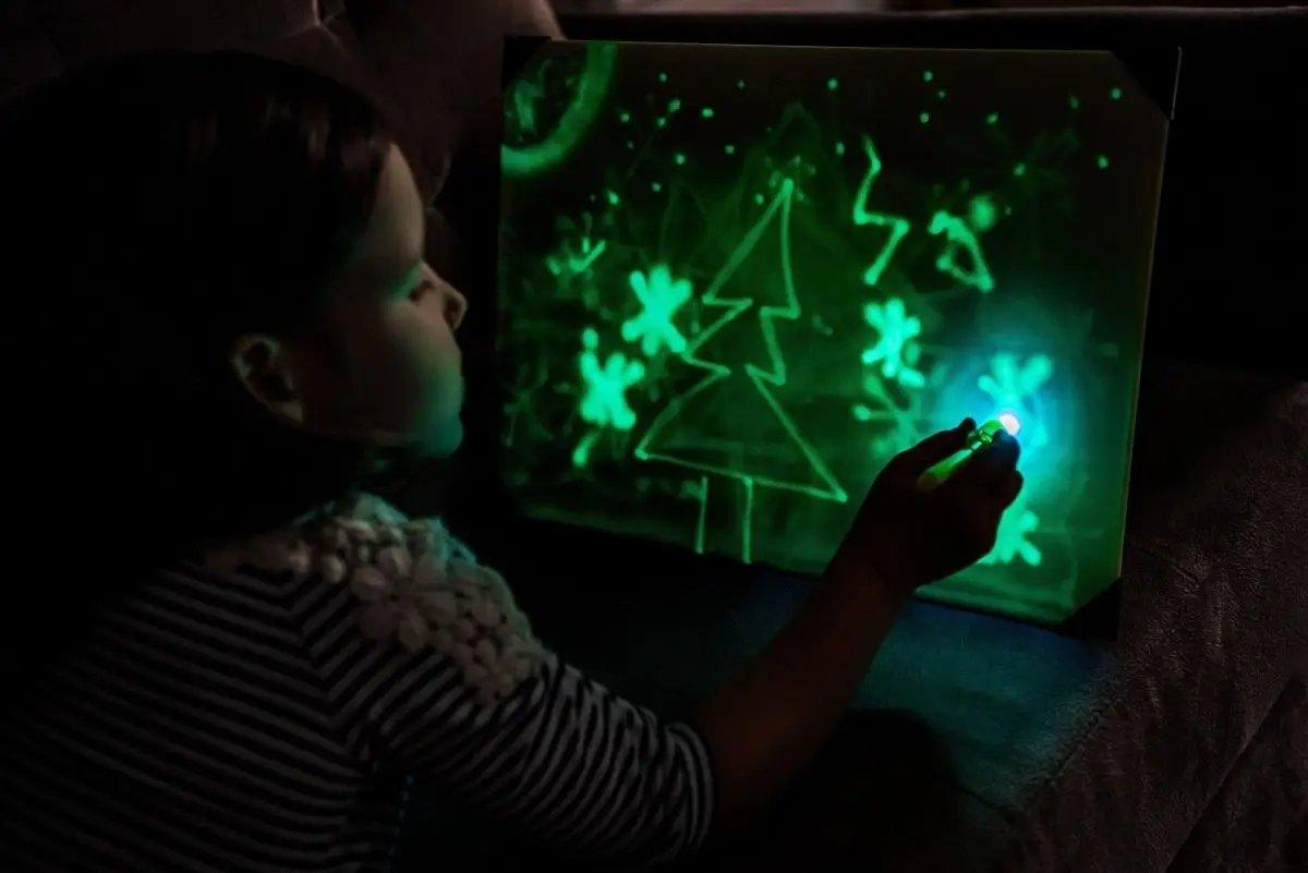 Child drawing a glowing tree on a light-up sketch board, showcasing creativity and imagination.