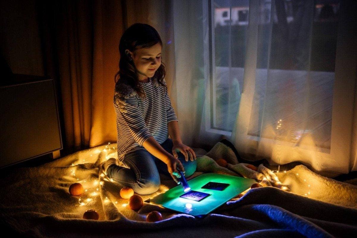 Child using a glowing drawing board in a cozy room, creating art at night with soft lights illuminating the scene.