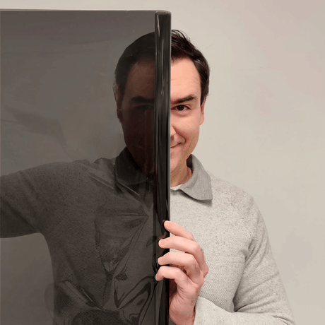 Ein Mann hält eine Rolle dunkler Tönungsfolie vor sein Gesicht, ein Teil seines Gesichts ist durch die Folie zu sehen.