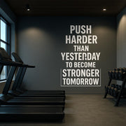 Gym wall decal with motivational quote: 'Push Harder Than Yesterday to Become Stronger Tomorrow' in modern workout room.