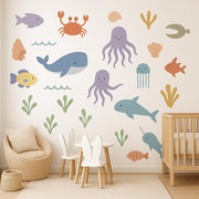 A nursery room wall decorated with colorful ocean-themed decals including whales, octopuses, fish, jellyfish, coral.