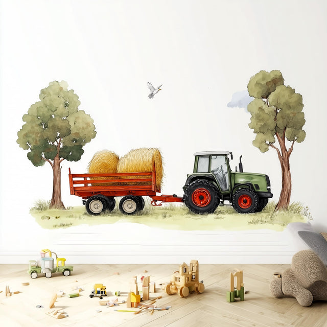 A playful wall decal featuring a green farm tractor pulling a trailer with hay bales between two trees, placed in a child's room above a wooden floor with toy blocks and trucks scattered around.