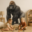 A children's playroom with a large, realistic gorilla wall decal on a beige wall; two young kids sit on a circular rug playing with jungle animal figurines in front of the decal.
