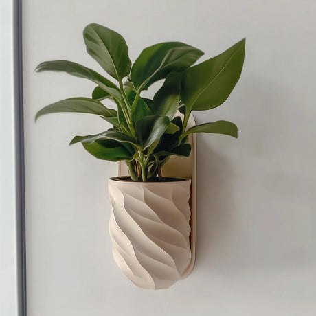 A beige, spiral-textured 3D printed planter mounted on a wall, holding a leafy green indoor plant. The design is smooth, modern, and minimalist, blending function with decor.