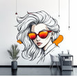 A modern wall decal featuring a stylized woman with white flowing hair and red-orange reflective sunglasses, in a bold comic book design above a monochrome cabinet in a contemporary room.